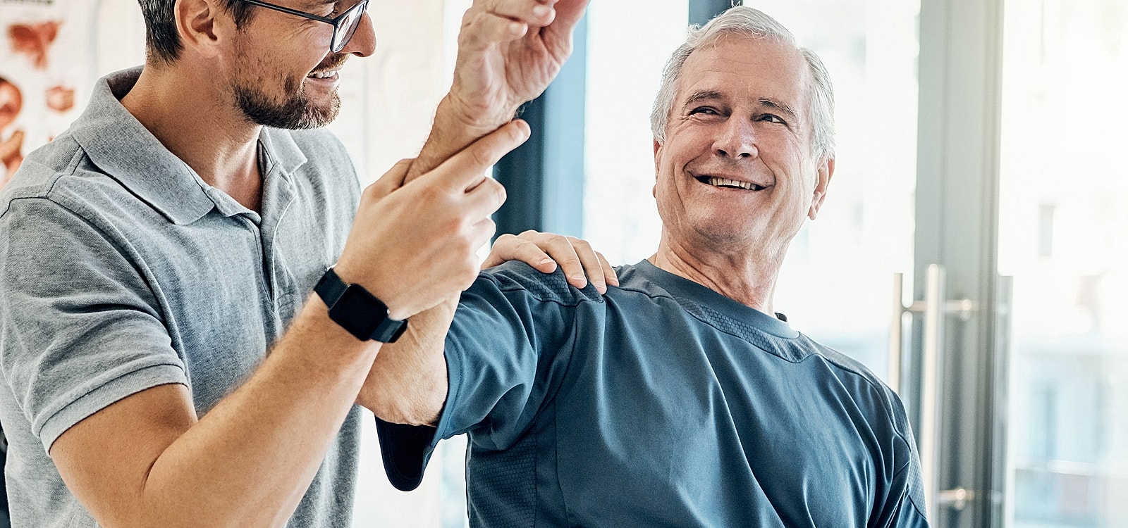 Therapist assisting elderly man with shoulder exercise.