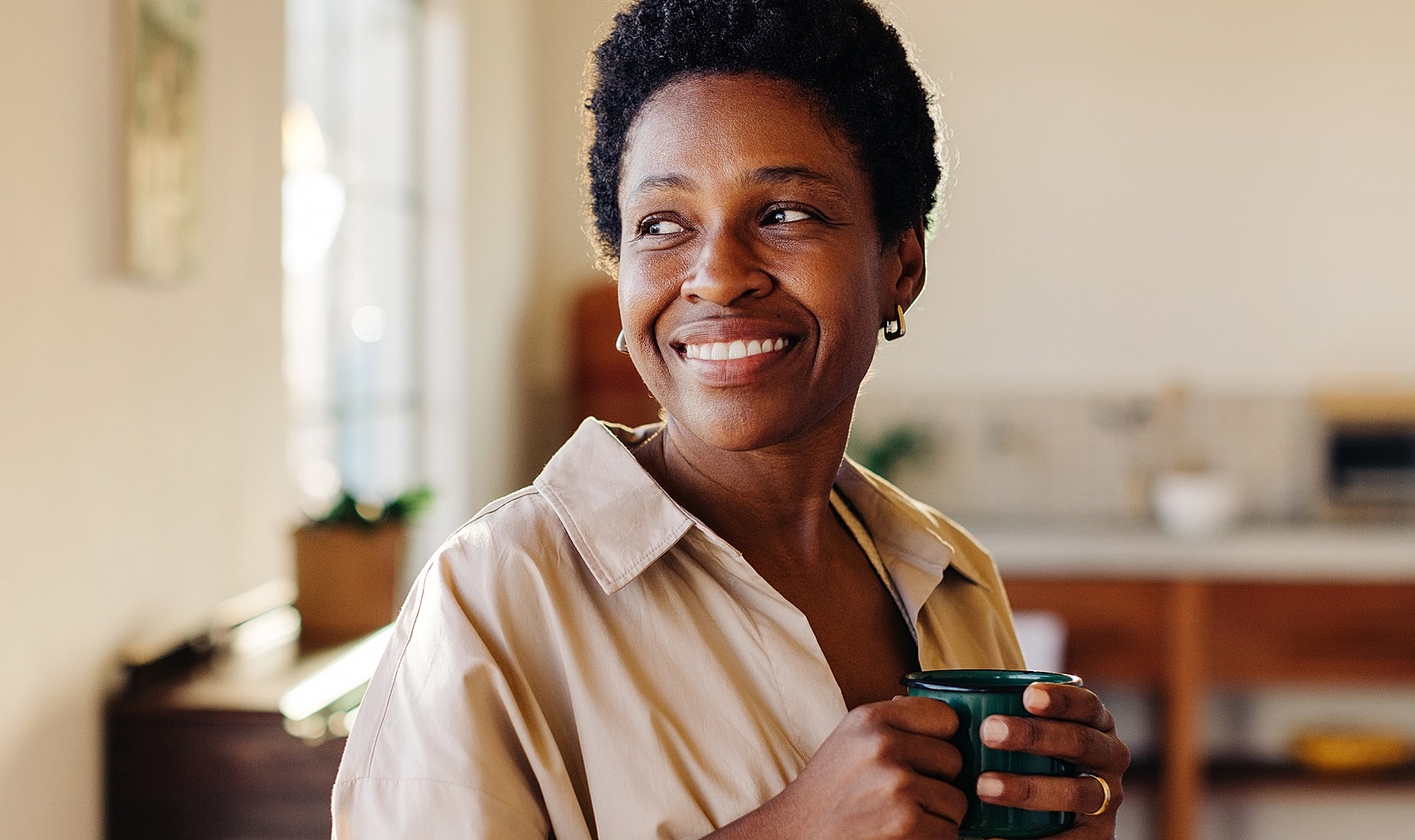 Smiling woman holding a cup in bright kitchen.
